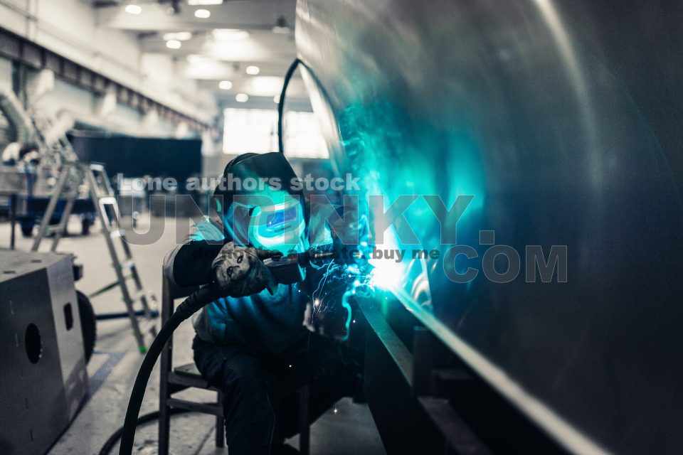 The worker makes spot welding of metal parts in the factory, sparks, and glow