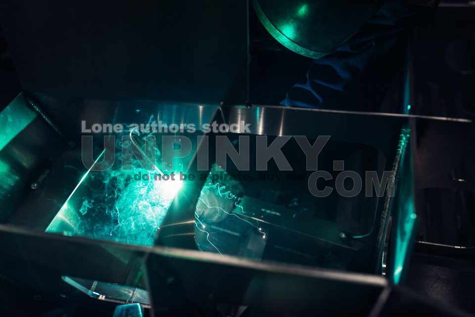 The worker makes spot welding of metal parts in the factory, sparks, and glow