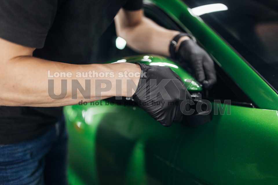 A man makes a detailing of a new car in good lighting, wrapping with a transparent protection film