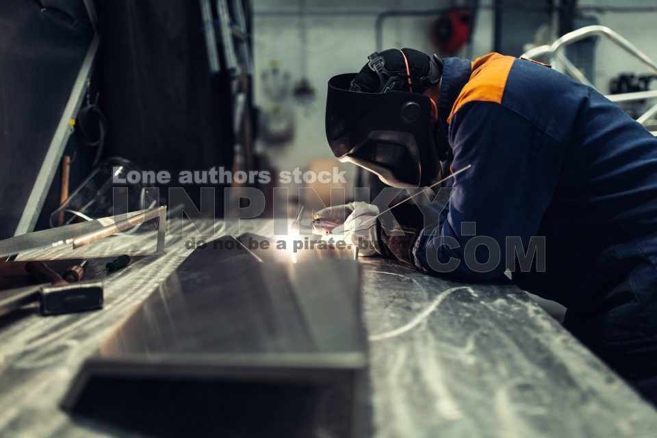 The master makes spot welding of metal parts in the factory, sparks, and glow