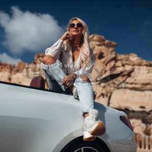 Young woman is sitting at the trunk of modern convertible car
