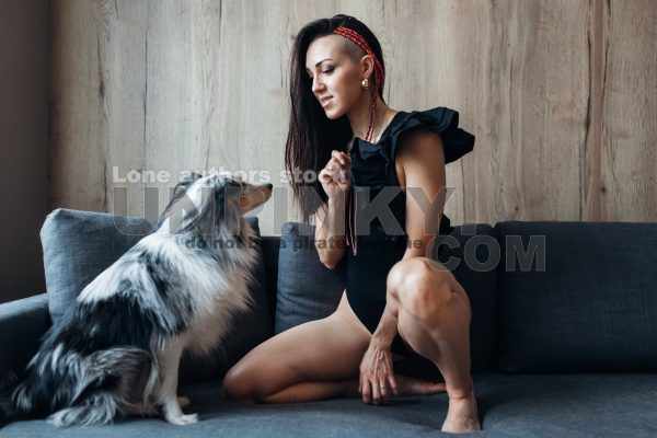 An attractive woman with long hair playing with an amstaff dog on the sofa. Young lady with a dog