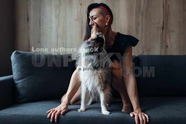 An attractive woman with long hair playing with an amstaff dog on the sofa. Young lady with a dog