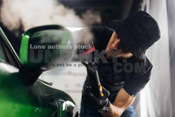 A man makes a detailing of a new car and use a steam to wrap a mirror
