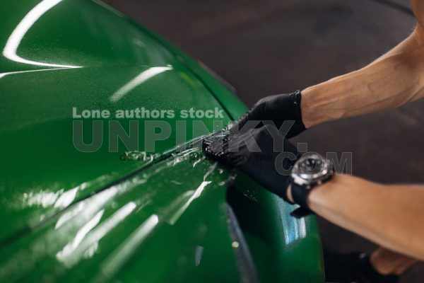 A man makes a detailing of a new car in good lighting, wrapping with a transparent protection film