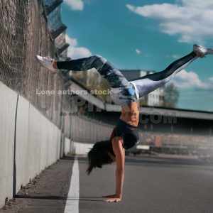 Beautiful girl teen doing a handstand on asphalt against blue sky and concrete wall