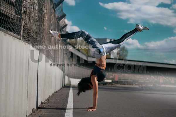 Beautiful girl teen doing a handstand on asphalt against blue sky and concrete wall