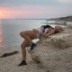 Beautiful sexy woman with waving hairs is sitting on the top of rock near ocean