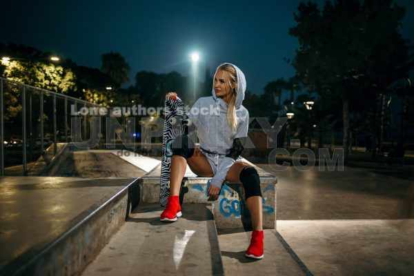 Girl holding a skateboard at night in the spotlights