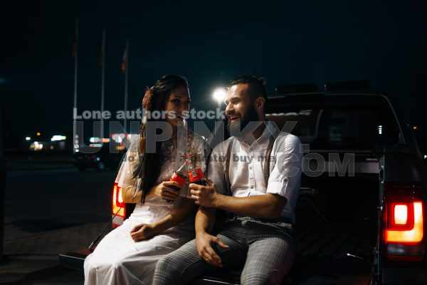 Modern hipster bride and groom is sitting in the car trunk. Wife and husband on the boot of car