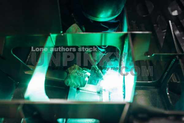 The master makes spot welding of metal parts in the factory, sparks, and glow. Man cut off metal construction