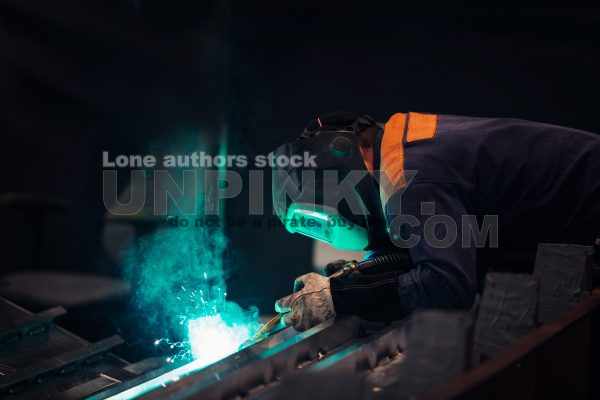 The master makes spot welding of metal parts in the factory, sparks, and glow