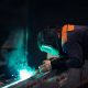 The master makes spot welding of metal parts in the factory, sparks, and glow