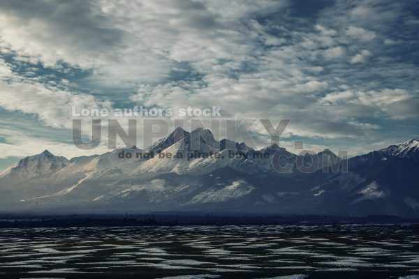 Snowy mountains in the distance. Dramatic view on winter landscape with mountains and rock, covered with snow. Heavy clouds above ski resort