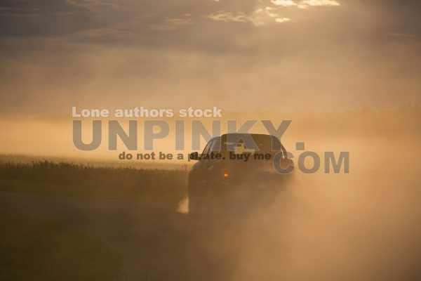 Pickup truck car in motion at the country road with clouds of dust. SUV car going fast on the dirt road at the sunset.