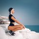 Beautiful woman with waving hairs is sitting on the top of rock near ocean