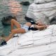 Beautiful sexy woman with waving hairs is sitting on the top of rock near ocean