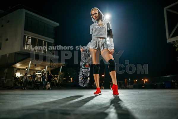 Girl holding a skateboard at night in the spotlights