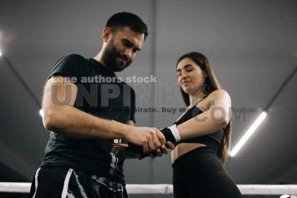 Trainer help to tape woman hand with a sport belt before kickbox
