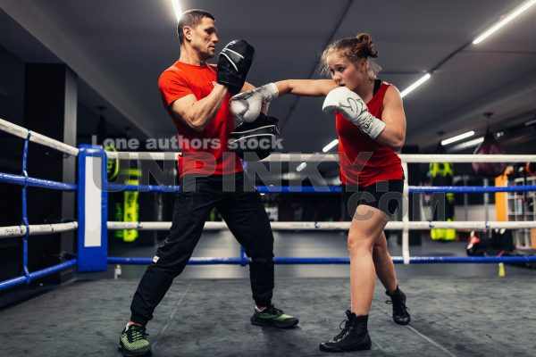 A girl in boxing training at the ring with a trainer