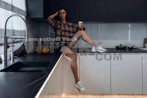 Stylish young woman relaxing in a modern kitchen with coffee in the morning. Modern kitchen with backlight. Lady is resting before working day