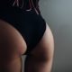 Beauty woman with attractive buttocks in black lingerie near the wall close up. Sexy and attractive woman with perfect skin