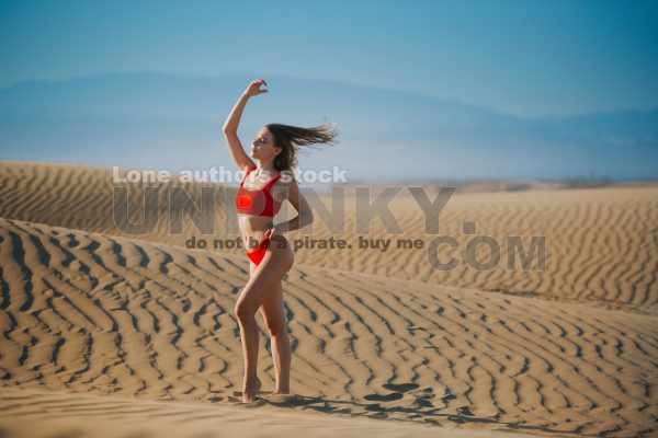 Beautiful fitness woman in red swimsuit is walking in the middle of desert