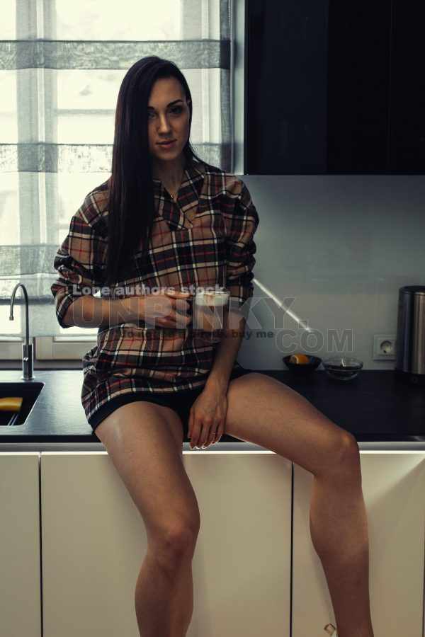 Stylish young woman relaxing in a modern kitchen with coffee in the morning. Modern kitchen with backlight. Lady is resting before working day