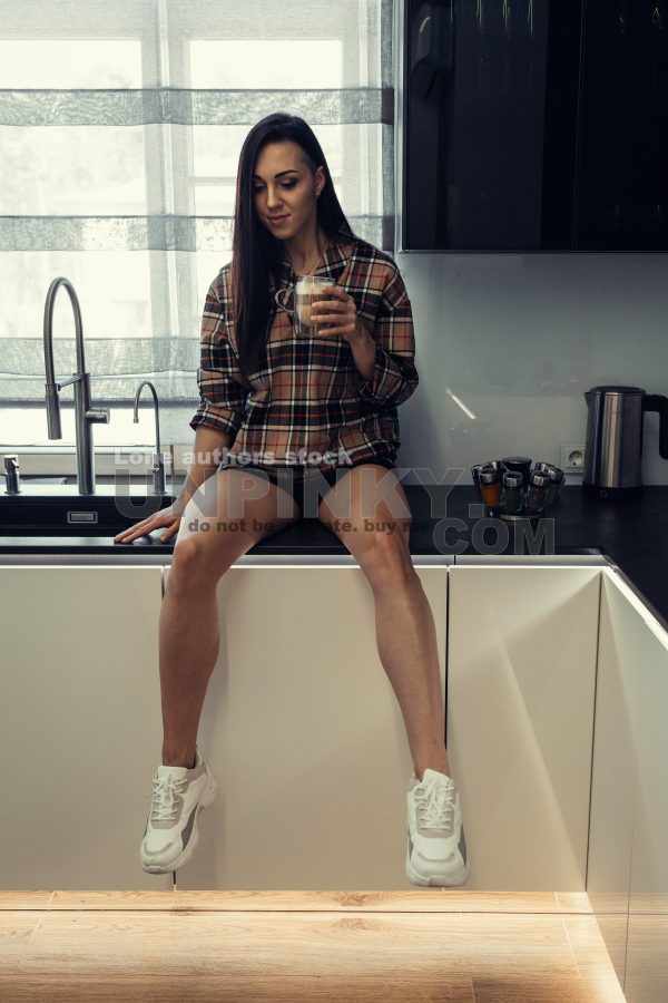 Stylish young woman relaxing in a modern kitchen with coffee in the morning. Modern kitchen with backlight. Lady is resting before working day