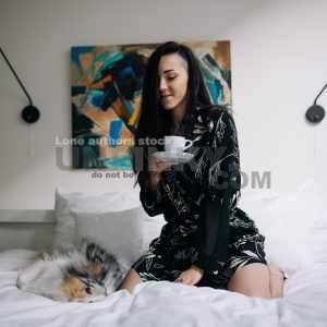 Attractive woman wakeup in the morning with a dog at the modern bright bedroom. Lady in a white hotel room