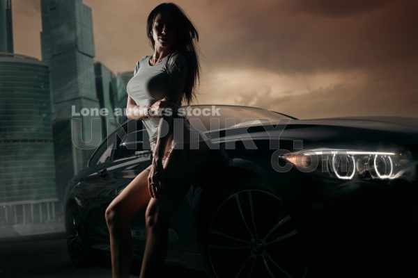 Fitness woman near BMW M4 sports coupe car in the evening in front of modern skyscrapers. Contrast shadows