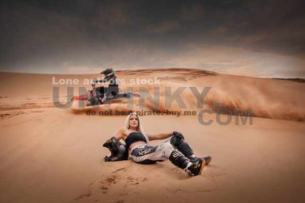 Woman with long hair sitting at the sands, and motorcycle rider go fast at the dune